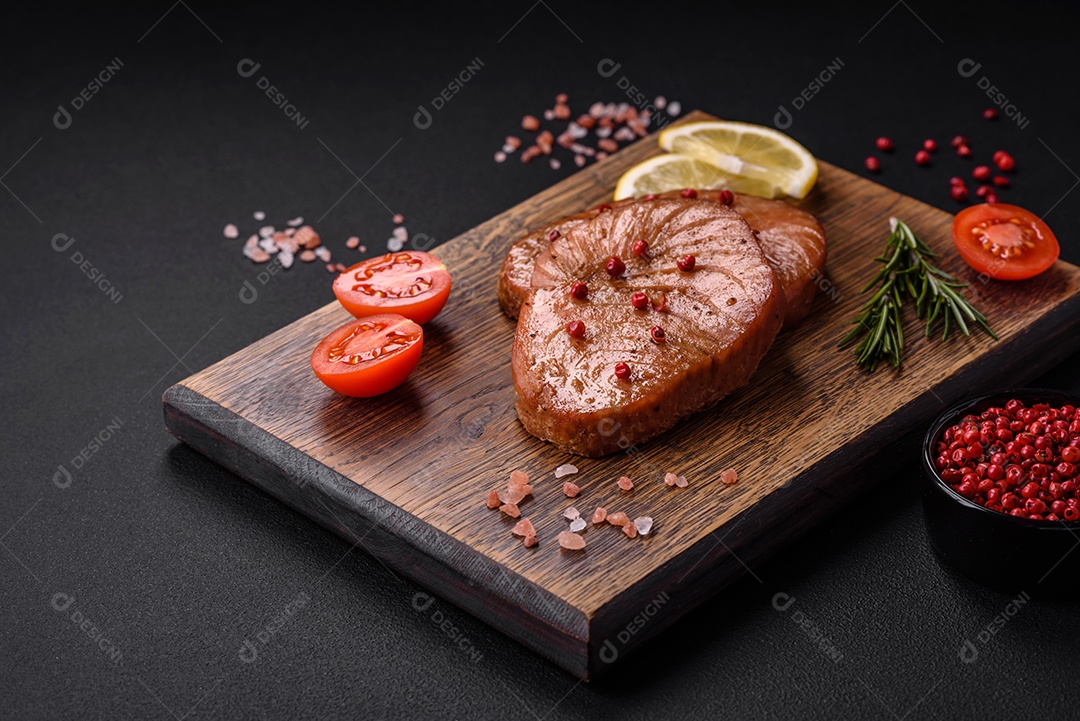 Duas fatias assadas de filé de atum com especiarias e ervas sobre um fundo escuro de concreto