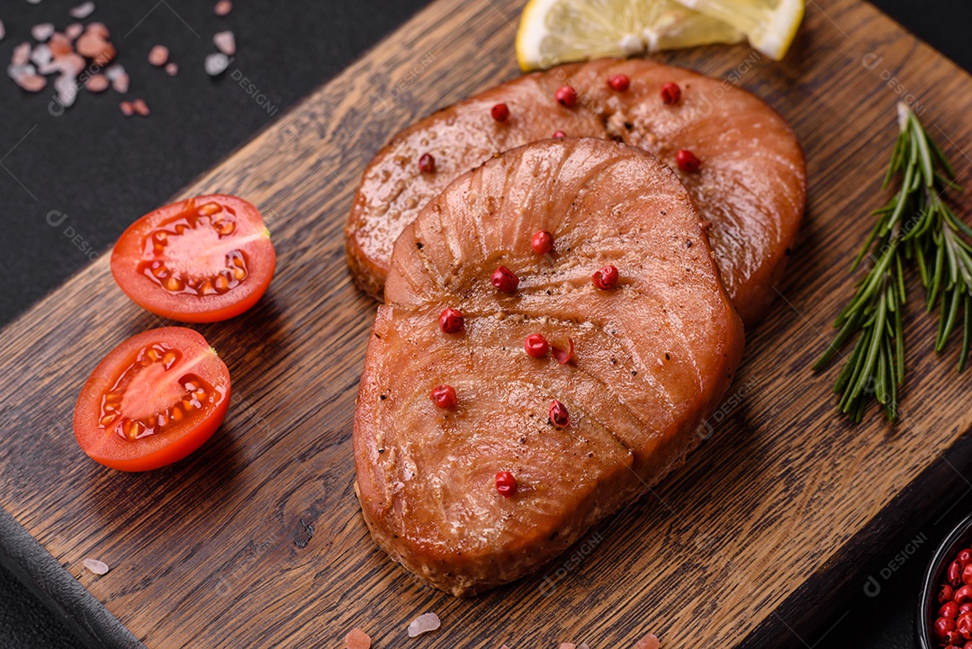 Duas fatias assadas de filé de atum com especiarias e ervas sobre um fundo escuro de concreto
