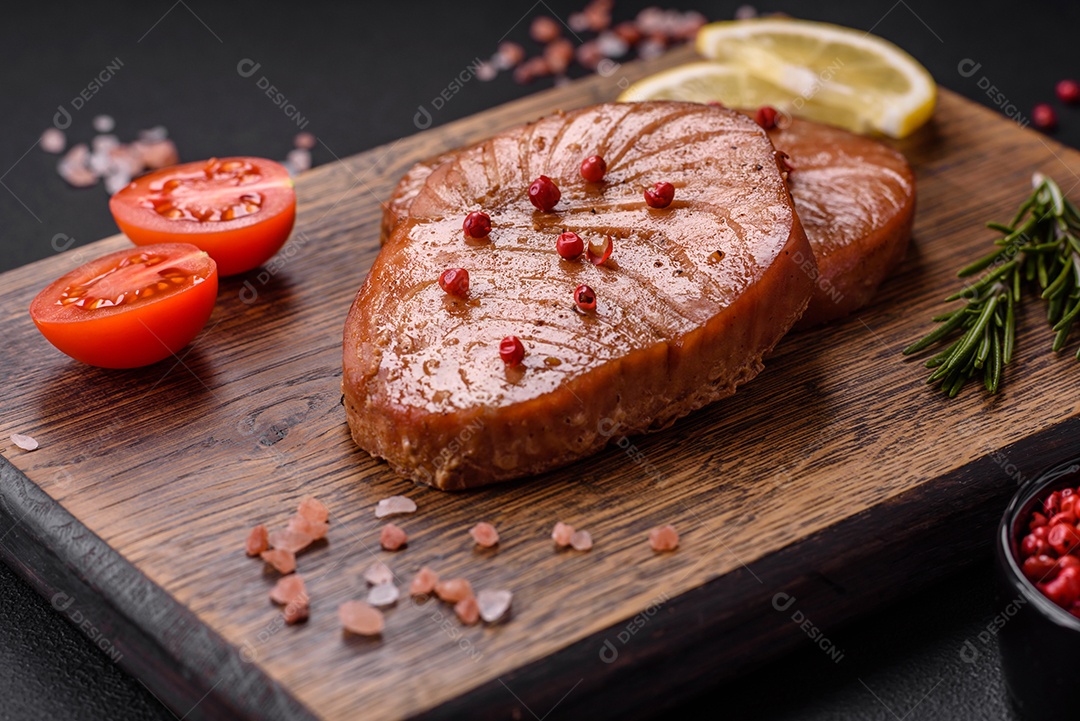 Duas fatias assadas de filé de atum com especiarias e ervas sobre um fundo escuro de concreto