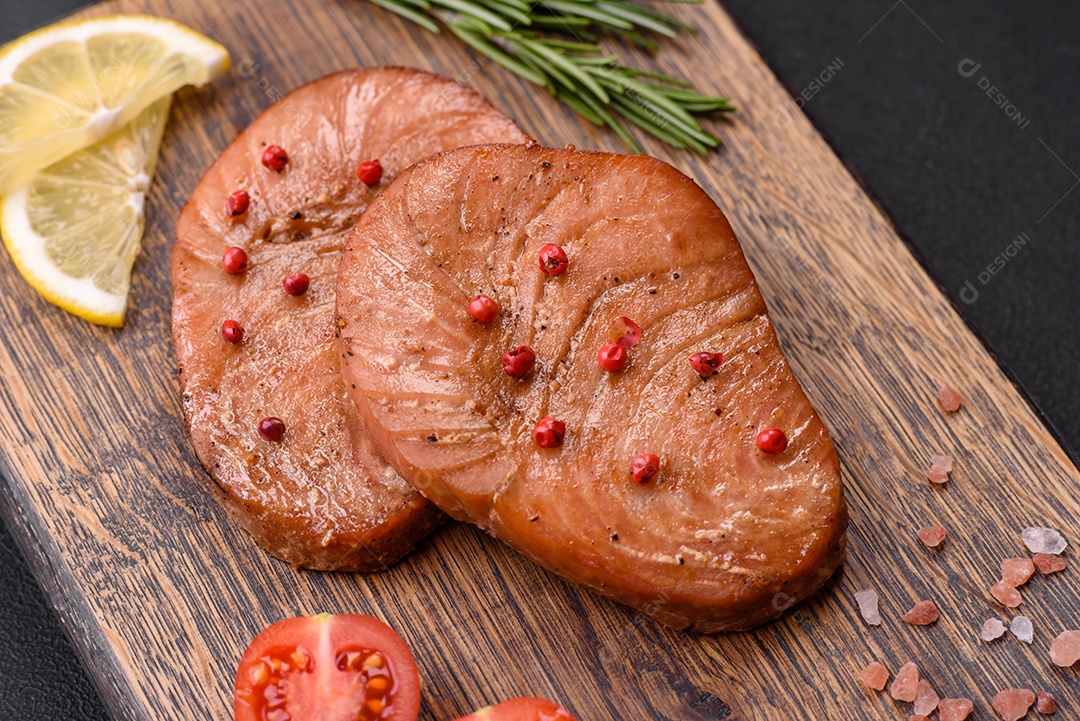 Duas fatias assadas de filé de atum com especiarias e ervas sobre um fundo escuro de concreto