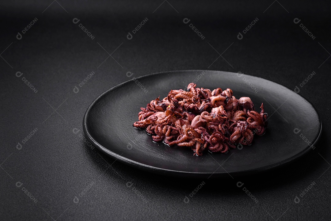 Deliciosos bebês polvos marinados com limão, sal e especiarias em uma placa preta sobre um fundo escuro de concreto