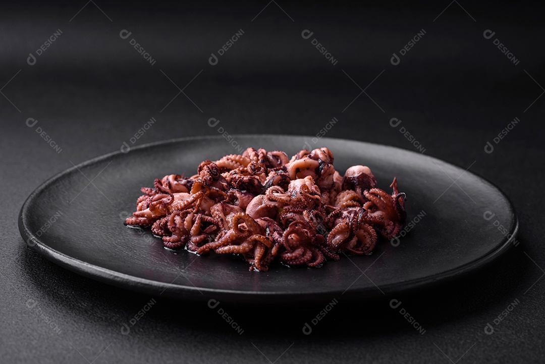 Deliciosos bebês polvos marinados com limão, sal e especiarias em uma placa preta sobre um fundo escuro de concreto