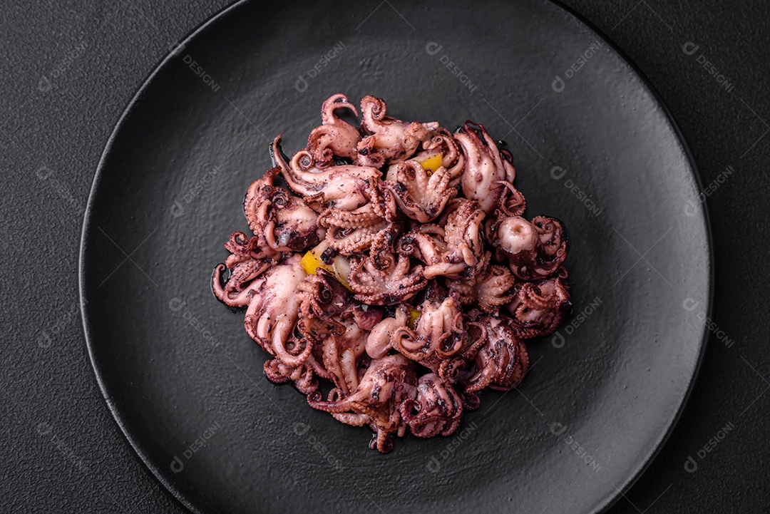 Deliciosos bebês polvos marinados com limão, sal e especiarias em uma placa preta sobre um fundo escuro de concreto