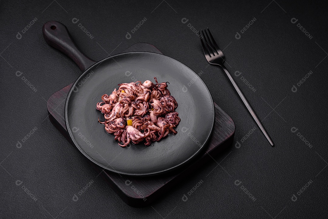 Deliciosos bebês polvos marinados com limão, sal e especiarias em uma placa preta sobre um fundo escuro de concreto