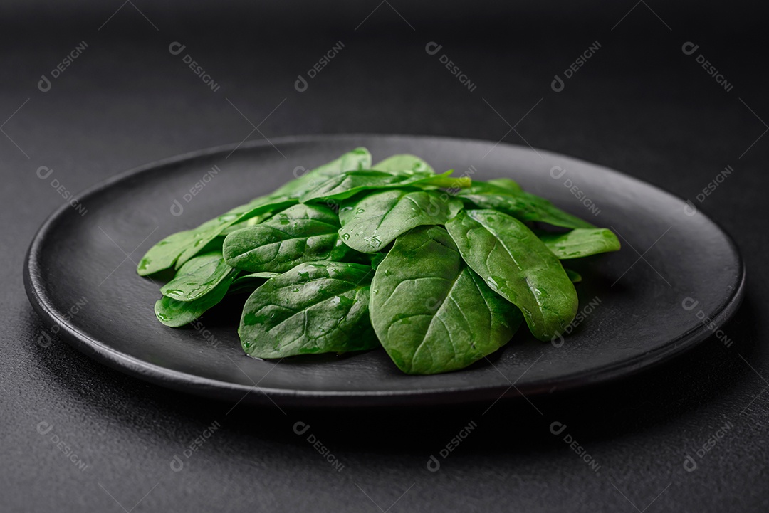 Folhas verdes frescas de espinafre em uma placa de cerâmica preta sobre um fundo escuro de concreto