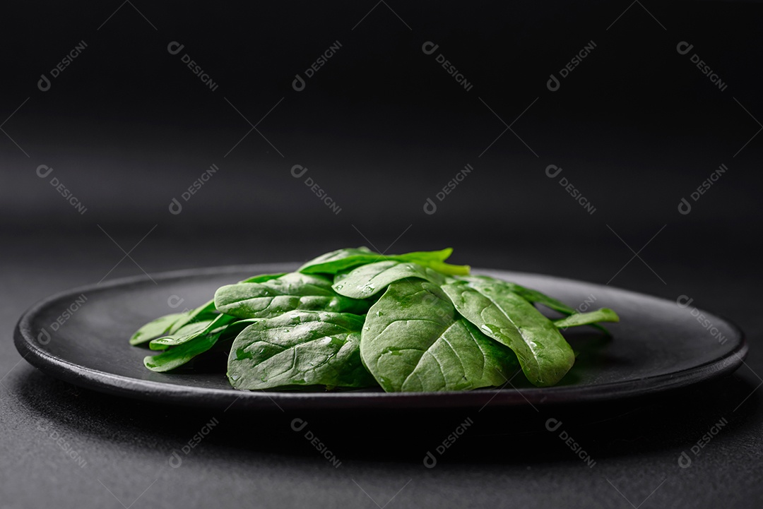Folhas verdes frescas de espinafre em uma placa de cerâmica preta sobre um fundo escuro de concreto