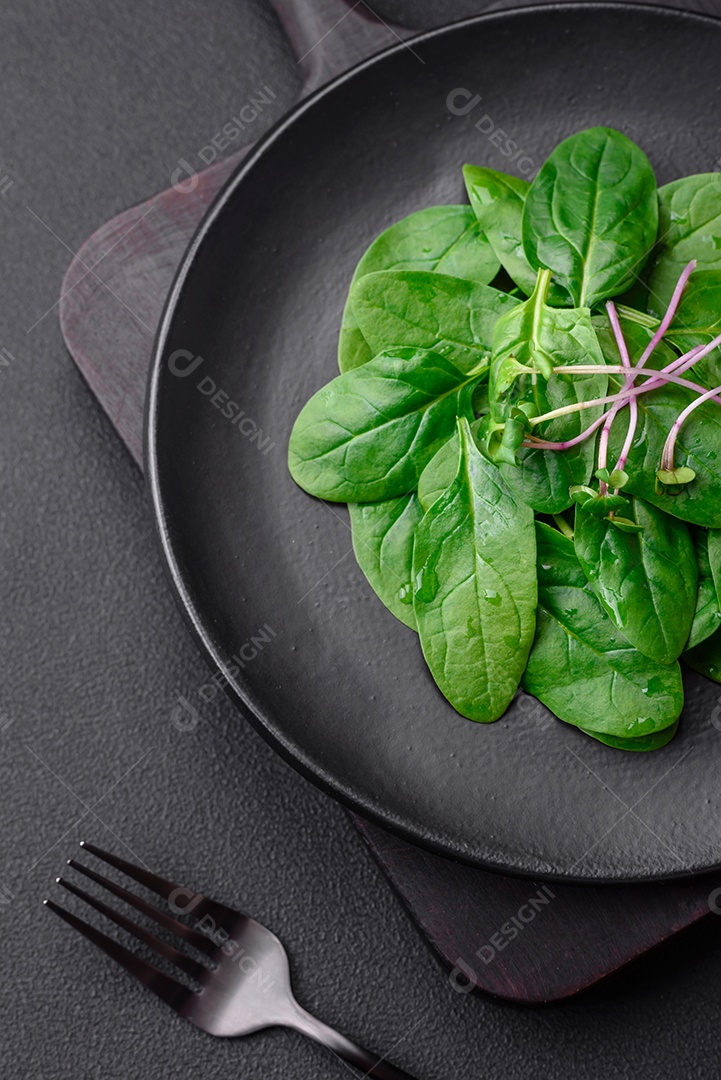 Folhas verdes frescas de espinafre em uma placa de cerâmica preta sobre um fundo escuro de concreto