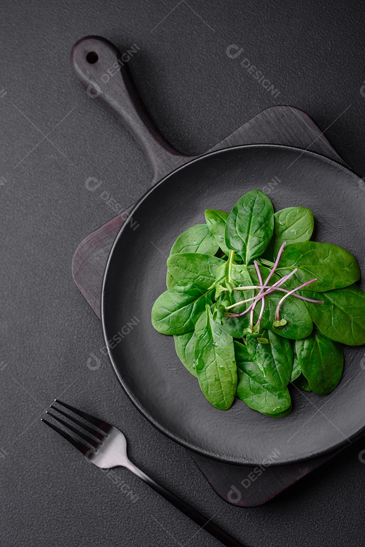 Folhas verdes frescas de espinafre em uma placa de cerâmica preta sobre um fundo escuro de concreto
