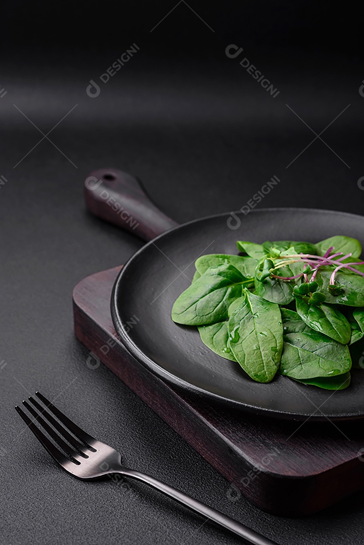 Folhas verdes frescas de espinafre em uma placa de cerâmica preta sobre um fundo escuro de concreto