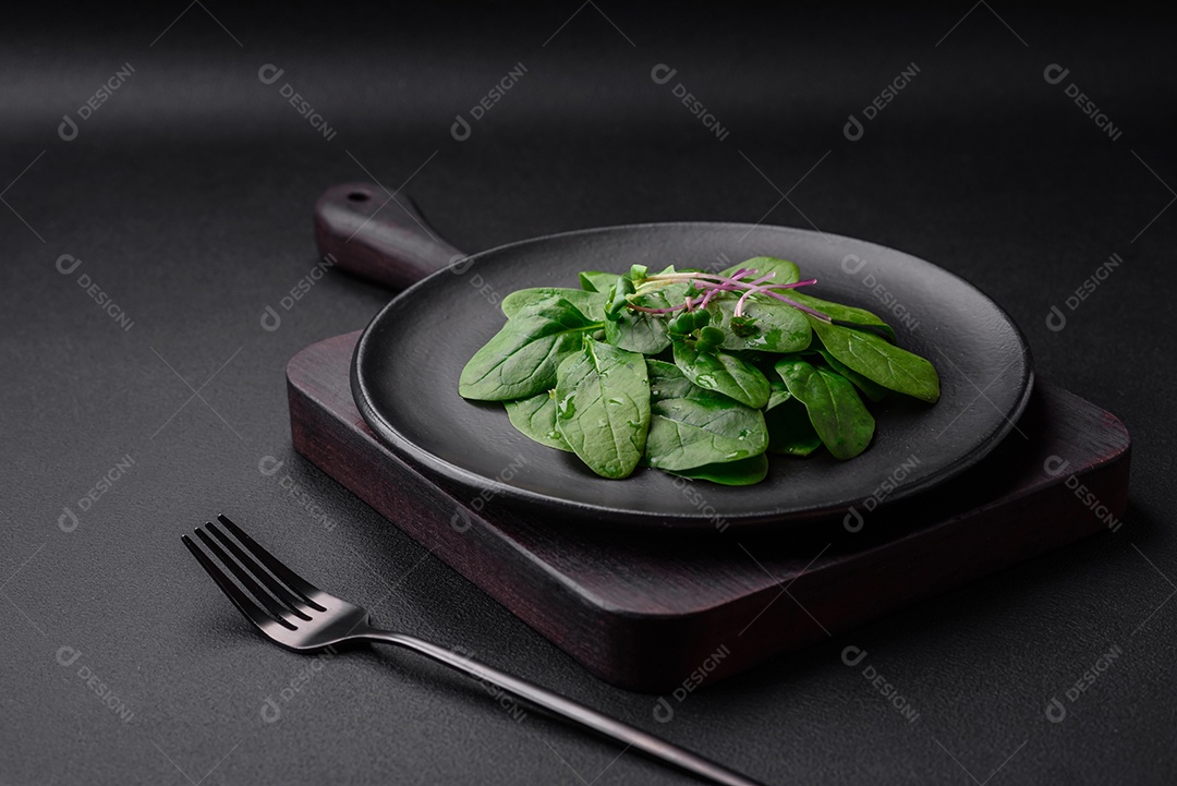 Folhas verdes frescas de espinafre em uma placa de cerâmica preta sobre um fundo escuro de concreto