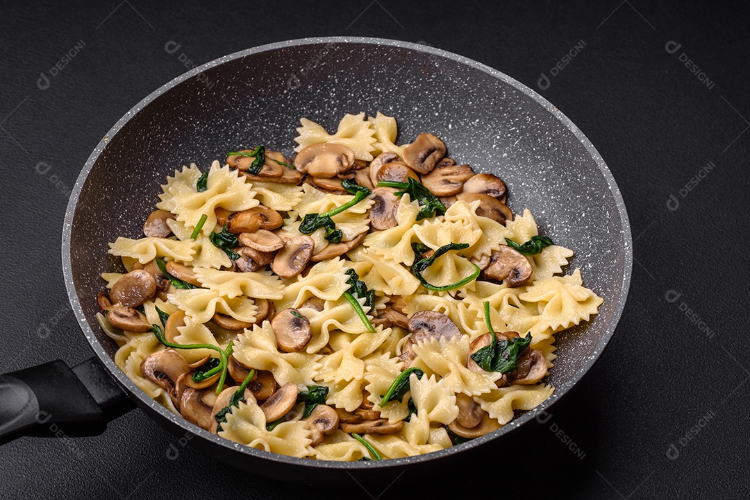 Deliciosa massa farfalle com cogumelos, queijo e espinafre com especiarias em uma placa preta sobre um fundo escuro de concreto