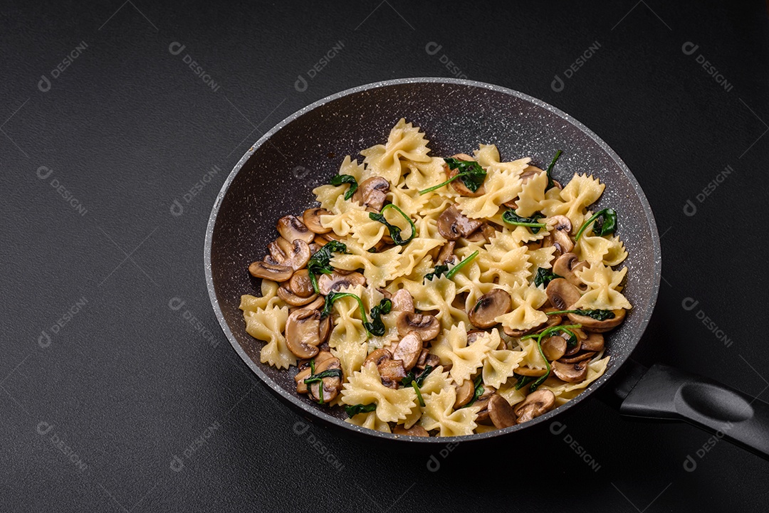 Deliciosa massa farfalle com cogumelos, queijo e espinafre com especiarias em uma placa preta sobre um fundo escuro de concreto