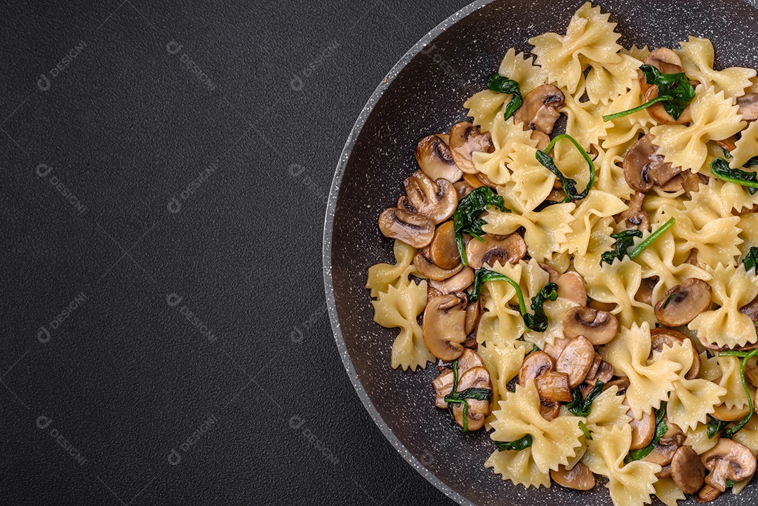Deliciosa massa farfalle com cogumelos, queijo e espinafre com especiarias em uma placa preta sobre um fundo escuro de concreto