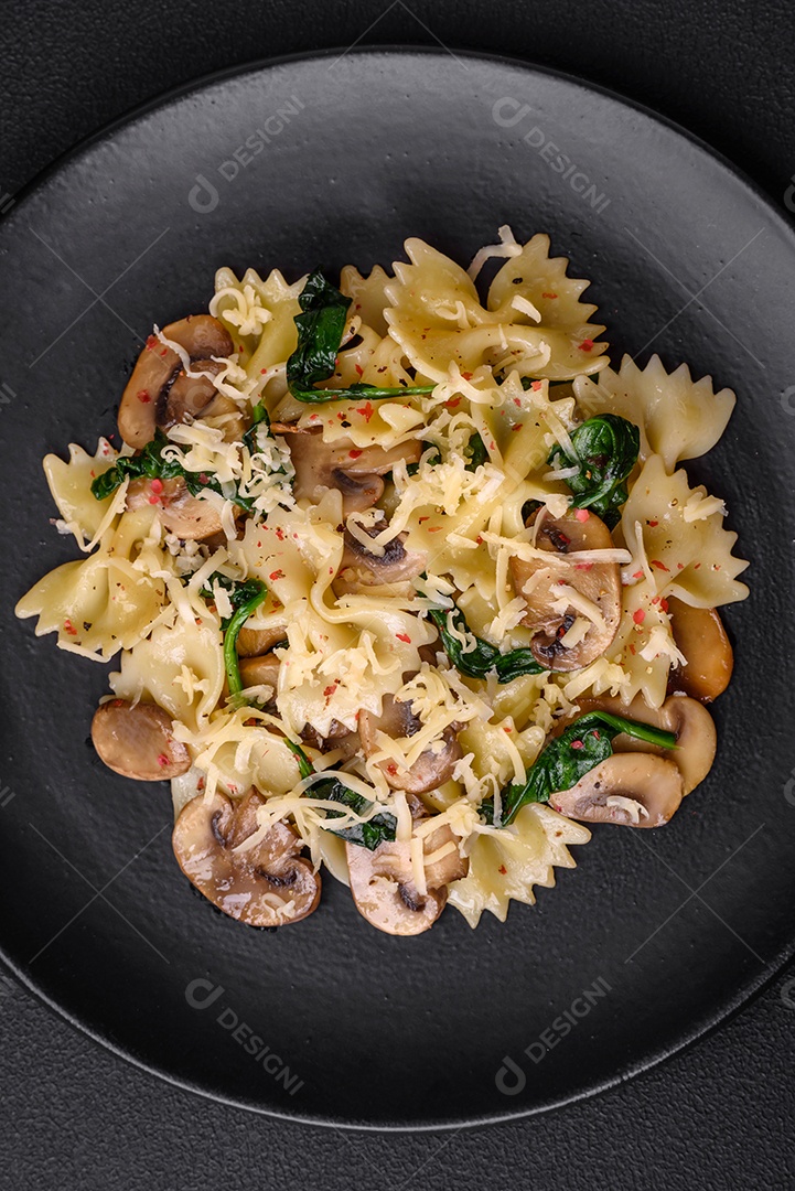 Deliciosa massa farfalle com cogumelos, queijo e espinafre com especiarias em uma placa preta sobre um fundo escuro de concreto