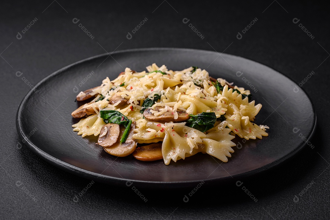 Deliciosa massa farfalle com cogumelos, queijo e espinafre com especiarias em uma placa preta sobre um fundo escuro de concreto