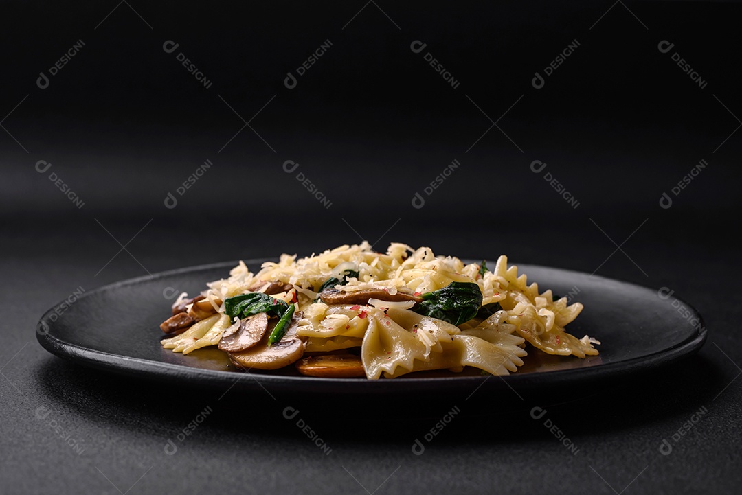 Deliciosa massa farfalle com cogumelos, queijo e espinafre com especiarias em uma placa preta sobre um fundo escuro de concreto