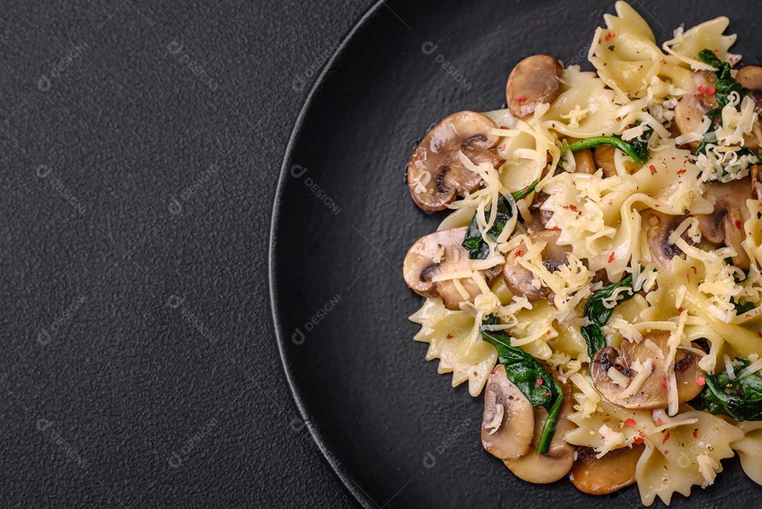 Deliciosa massa farfalle com cogumelos, queijo e espinafre com especiarias em uma placa preta sobre um fundo escuro de concreto