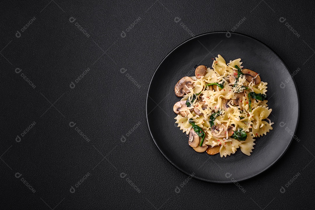 Deliciosa massa farfalle com cogumelos, queijo e espinafre com especiarias em uma placa preta sobre um fundo escuro de concreto