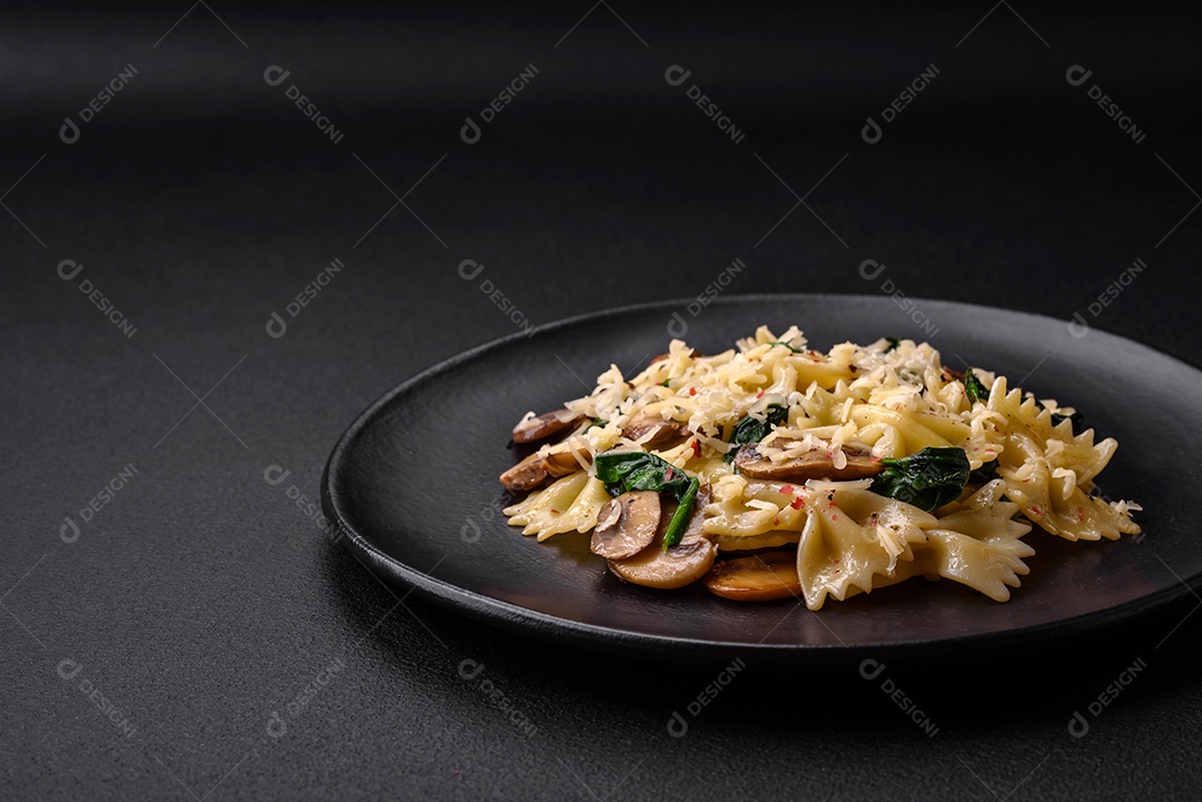 Deliciosa massa farfalle com cogumelos, queijo e espinafre com especiarias em uma placa preta sobre um fundo escuro de concreto