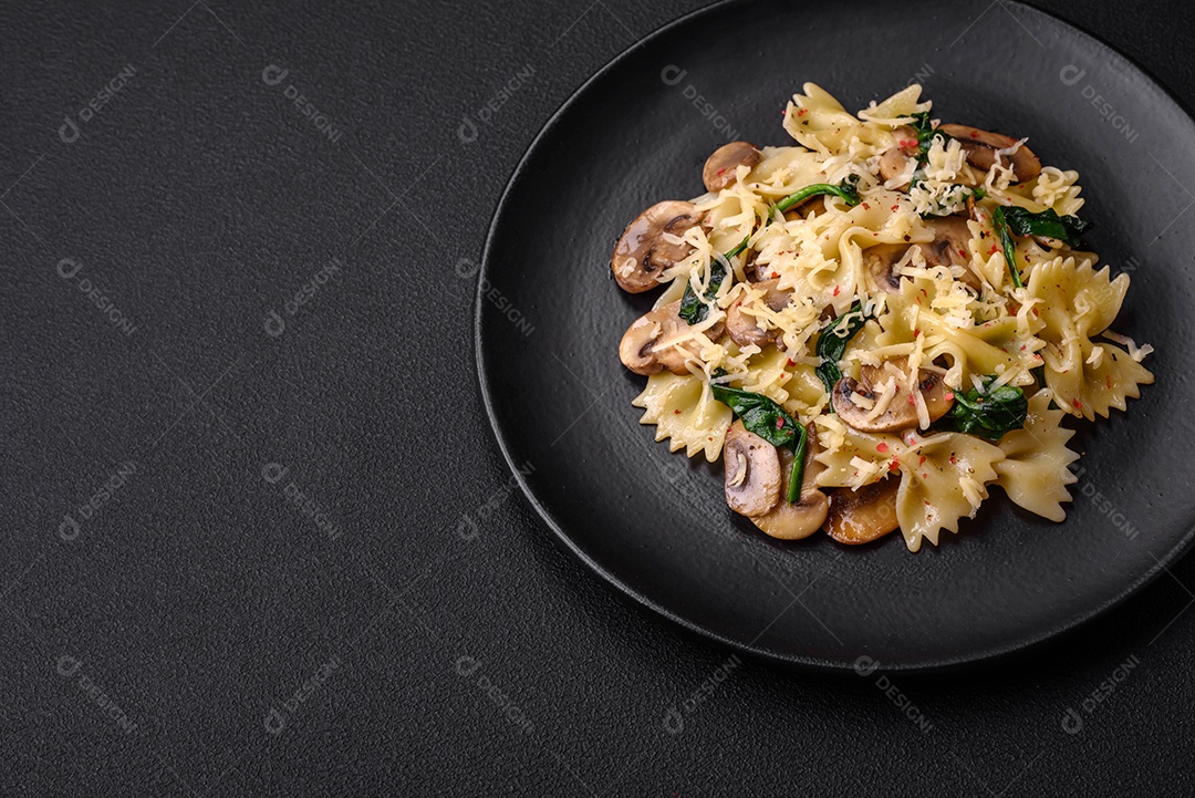 Deliciosa massa farfalle com cogumelos, queijo e espinafre com especiarias em uma placa preta sobre um fundo escuro de concreto