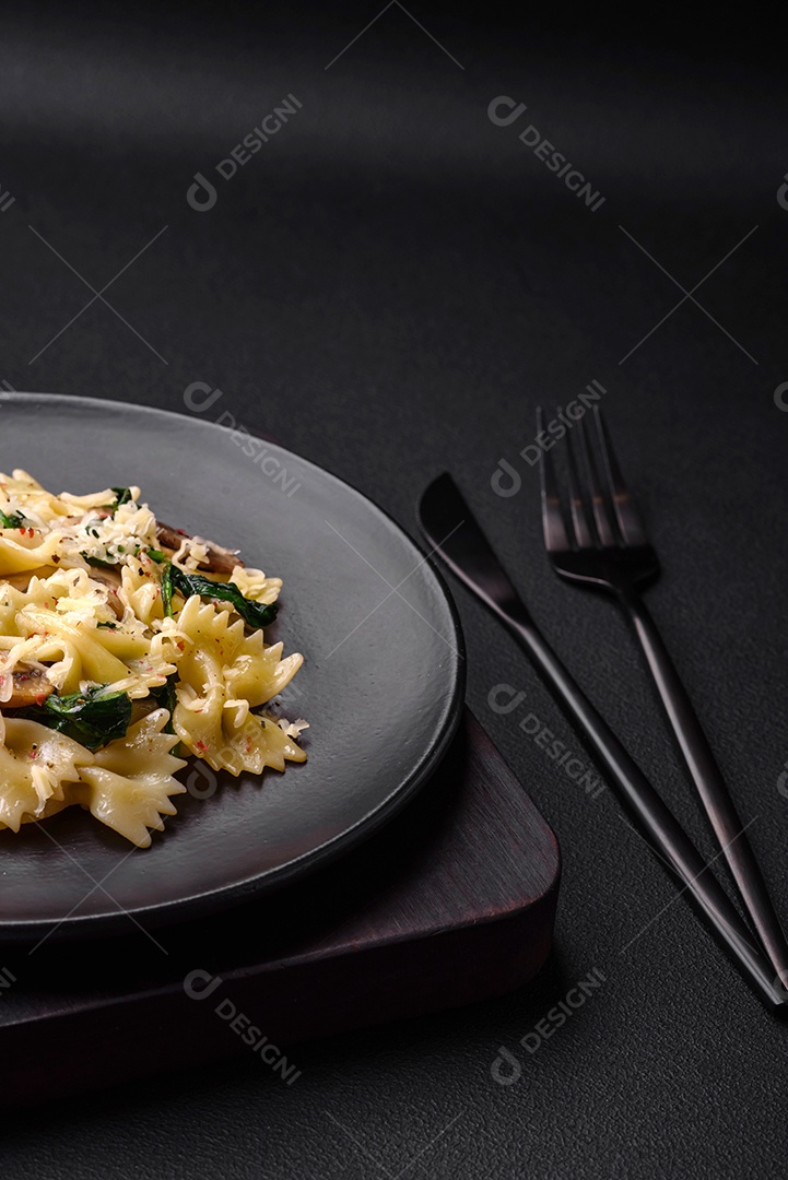 Deliciosa massa farfalle com cogumelos, queijo e espinafre com especiarias em uma placa preta sobre um fundo escuro de concreto