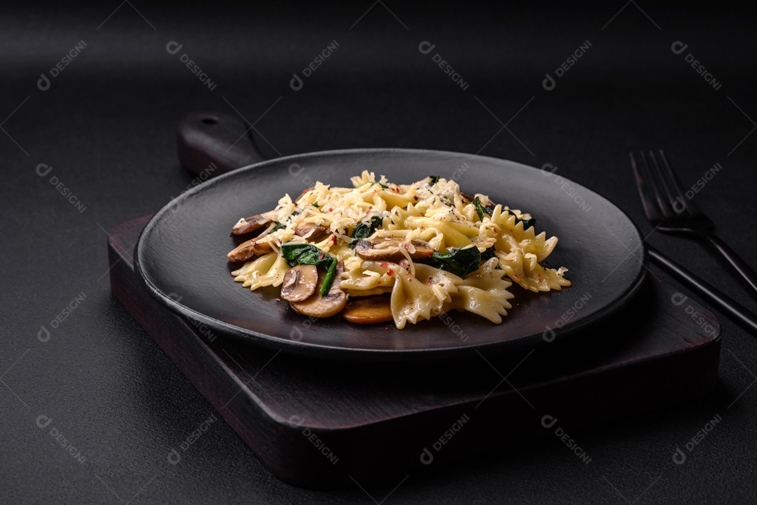 Deliciosa massa farfalle com cogumelos, queijo e espinafre com especiarias em uma placa preta sobre um fundo escuro de concreto