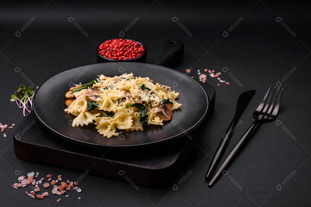 Deliciosa massa farfalle com cogumelos, queijo e espinafre com especiarias em uma placa preta sobre um fundo escuro de concreto