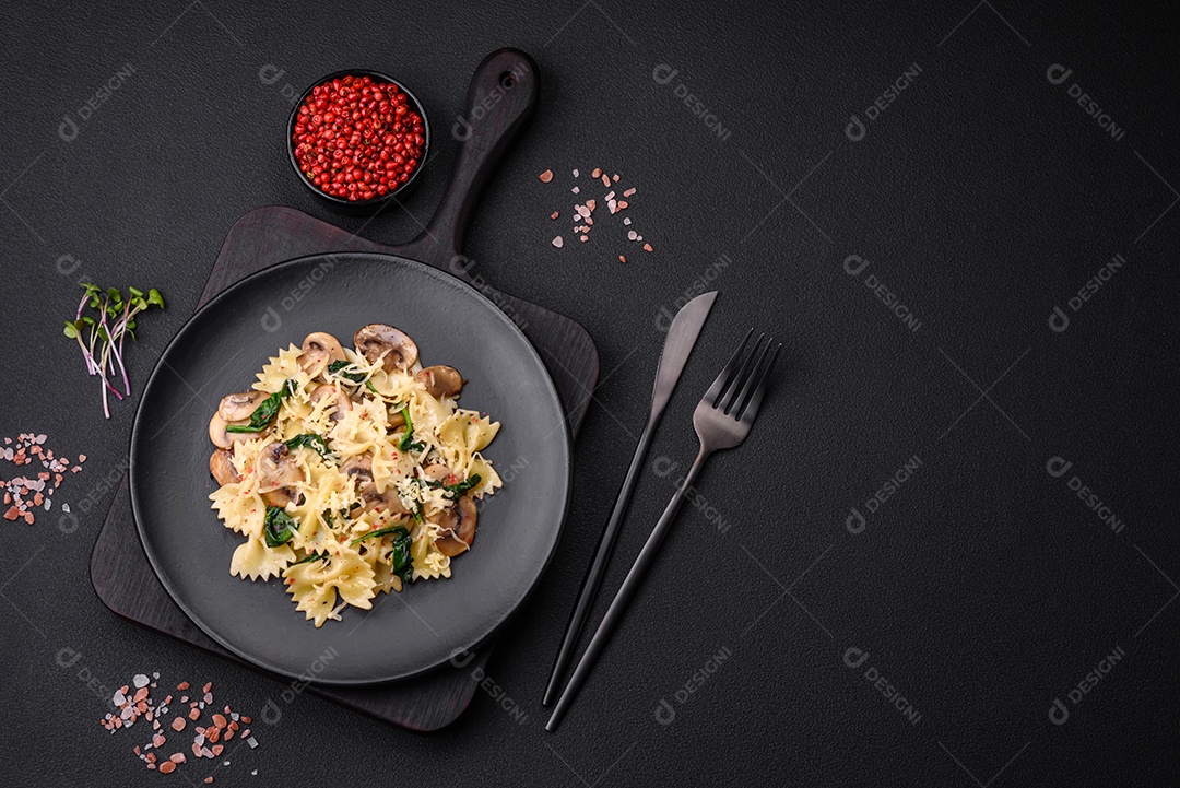 Deliciosa massa farfalle com cogumelos, queijo e espinafre com especiarias em uma placa preta sobre um fundo escuro de concreto