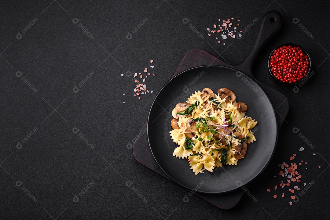 Deliciosa massa farfalle com cogumelos, queijo e espinafre com especiarias em uma placa preta sobre um fundo escuro de concreto