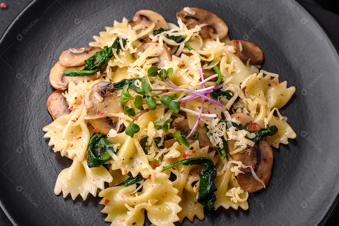 Deliciosa massa farfalle com cogumelos, queijo e espinafre com especiarias em uma placa preta sobre um fundo escuro de concreto