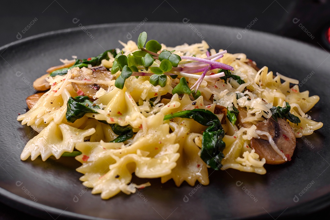 Deliciosa massa farfalle com cogumelos, queijo e espinafre com especiarias em uma placa preta sobre um fundo escuro de concreto