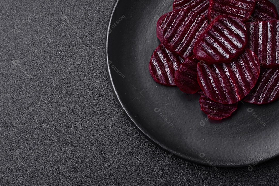 Deliciosas beterrabas de cor rubi cozidas e saudáveis ​​cortadas em uma placa preta sobre um fundo escuro de concreto