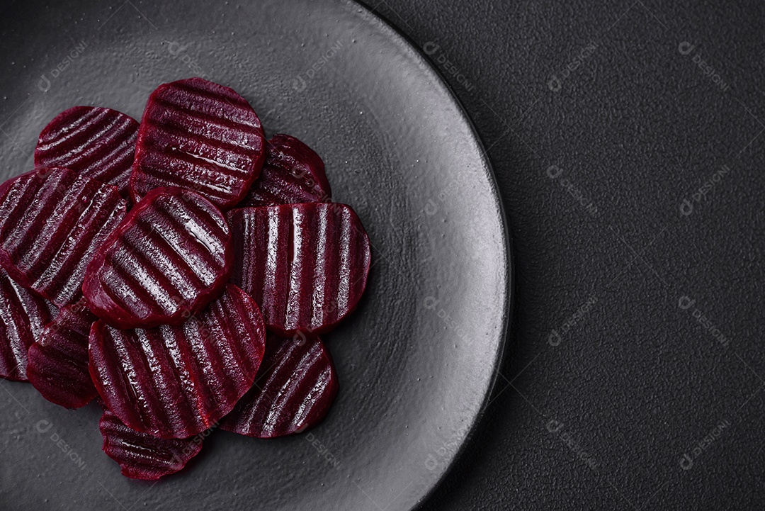 Deliciosas beterrabas de cor rubi cozidas e saudáveis ​​cortadas em uma placa preta sobre um fundo escuro de concreto