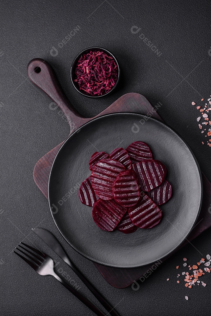 Deliciosas beterrabas de cor rubi cozidas e saudáveis ​​cortadas em uma placa preta sobre um fundo escuro de concreto