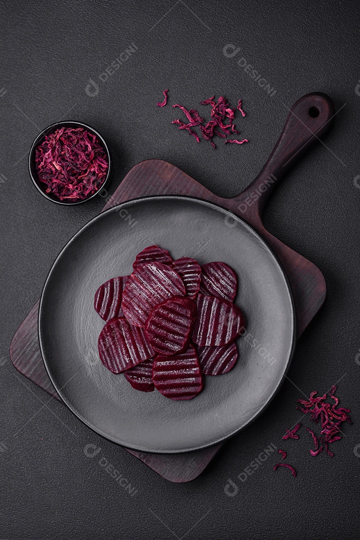 Deliciosas beterrabas de cor rubi cozidas e saudáveis ​​cortadas em uma placa preta sobre um fundo escuro de concreto