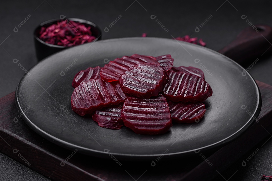 Deliciosas beterrabas de cor rubi cozidas e saudáveis ​​cortadas em uma placa preta sobre um fundo escuro de concreto