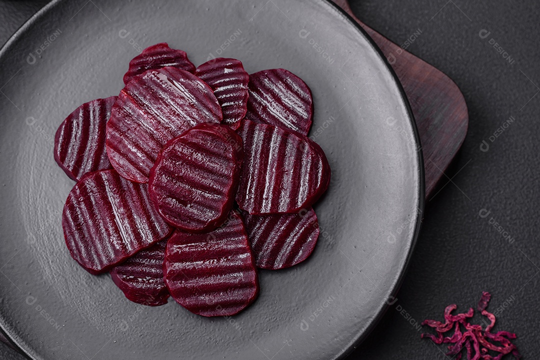 Deliciosas beterrabas de cor rubi cozidas e saudáveis ​​cortadas em uma placa preta sobre um fundo escuro de concreto