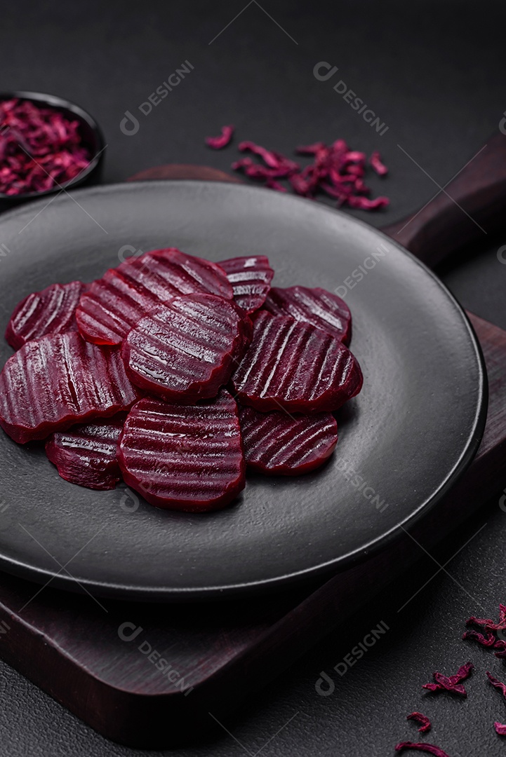 Deliciosas beterrabas de cor rubi cozidas e saudáveis ​​cortadas em uma placa preta sobre um fundo escuro de concreto