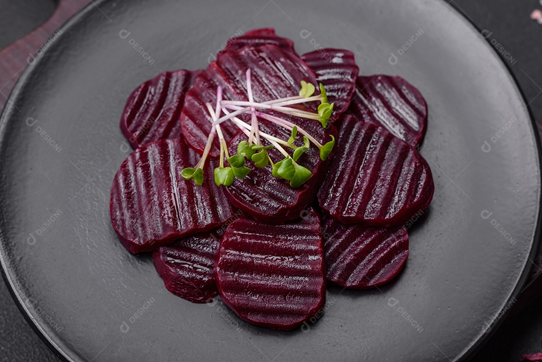 Deliciosas beterrabas de cor rubi cozidas e saudáveis ​​cortadas em uma placa preta sobre um fundo escuro de concreto