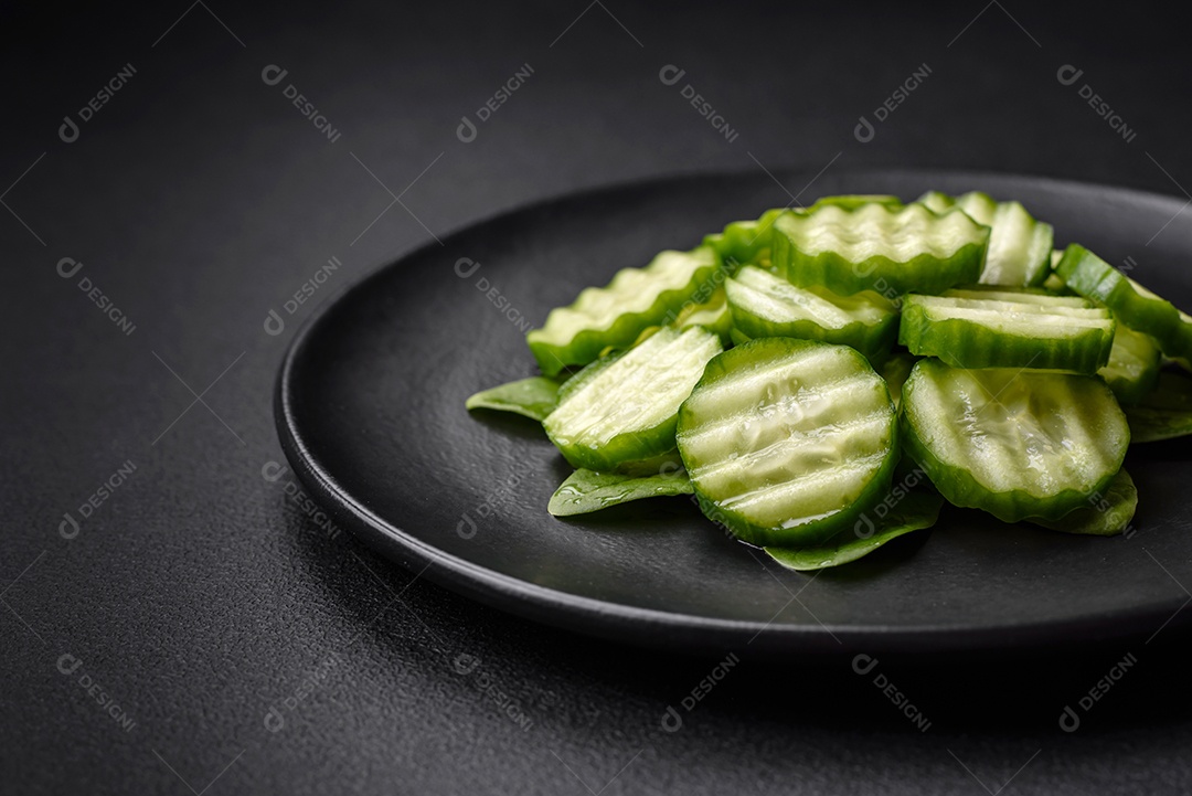 Delicioso pepino cru saudável cortado em uma placa de cerâmica preta sobre um fundo escuro de concreto
