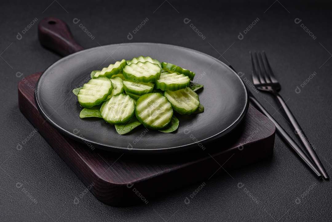 Delicioso pepino cru saudável cortado em uma placa de cerâmica preta sobre um fundo escuro de concreto