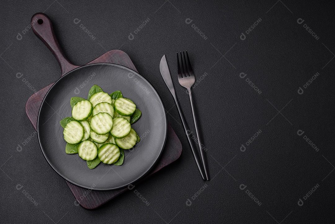 Delicioso pepino cru saudável cortado em uma placa de cerâmica preta sobre um fundo escuro de concreto