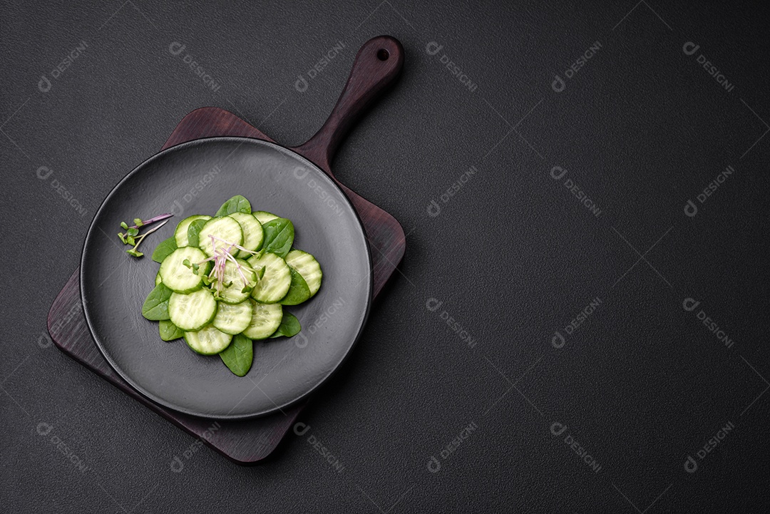 Delicioso pepino cru saudável cortado em uma placa de cerâmica preta sobre um fundo escuro de concreto