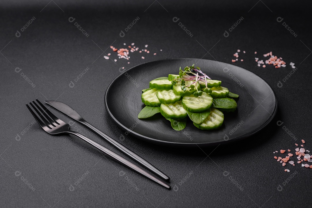 Delicioso pepino cru saudável cortado em uma placa de cerâmica preta sobre um fundo escuro de concreto