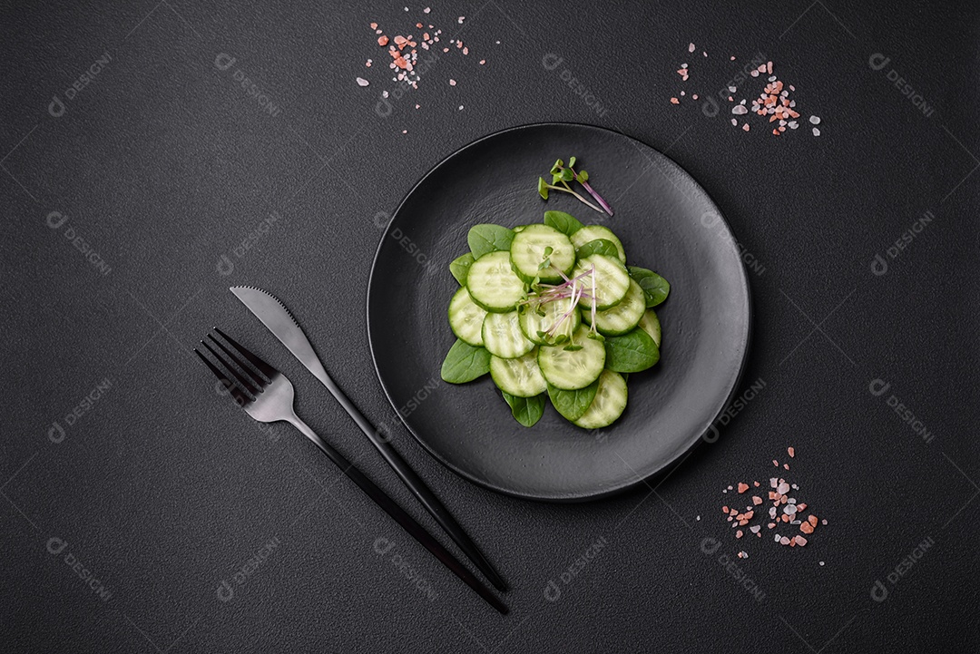 Delicioso pepino cru saudável cortado em uma placa de cerâmica preta sobre um fundo escuro de concreto
