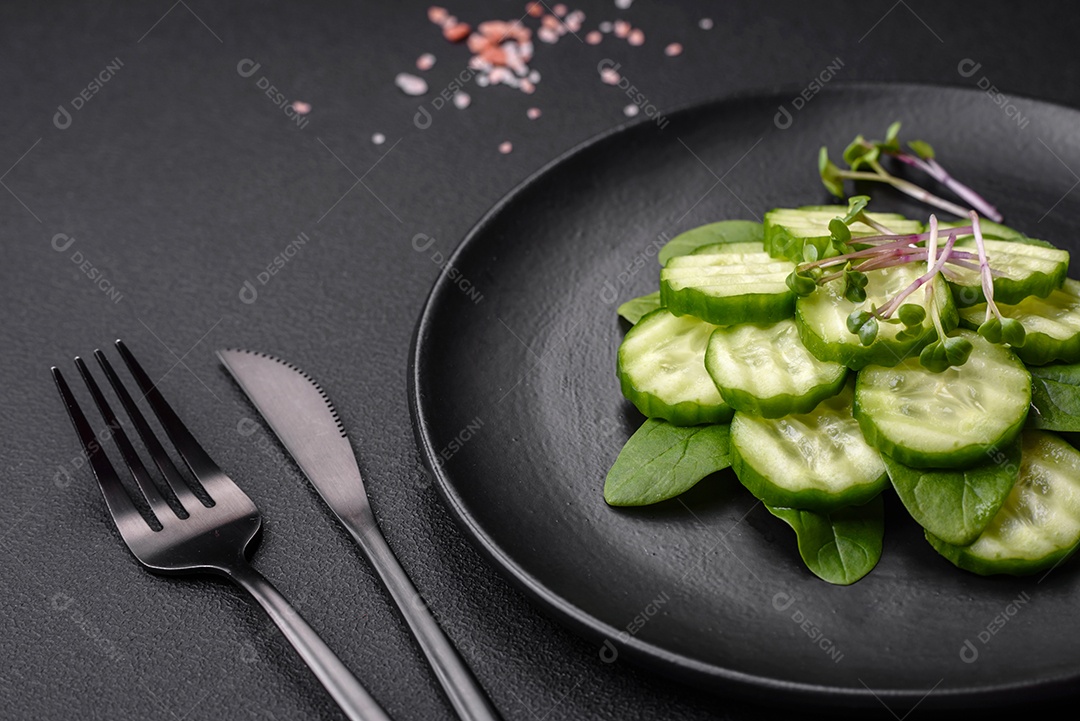 Delicioso pepino cru saudável cortado em uma placa de cerâmica preta sobre um fundo escuro de concreto