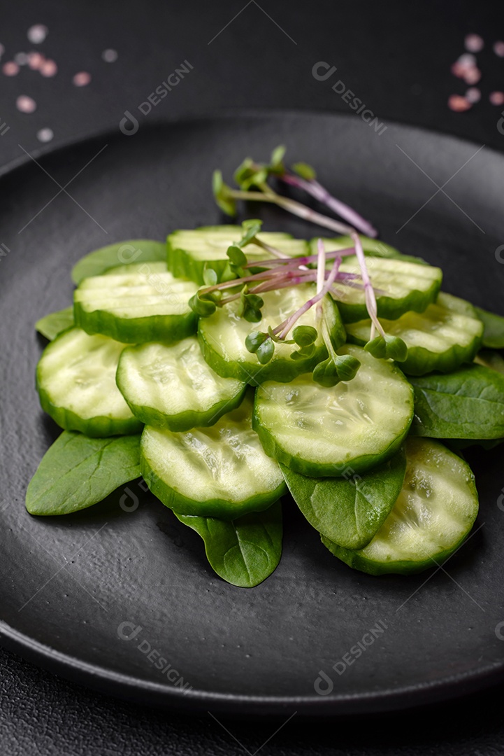Delicioso pepino cru saudável cortado em uma placa de cerâmica preta sobre um fundo escuro de concreto