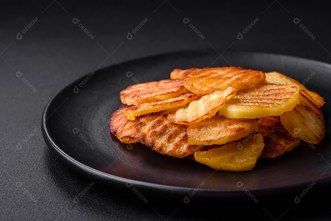 Deliciosas batatas fritas crocantes em fatias em uma placa de cerâmica preta sobre um fundo escuro de concreto