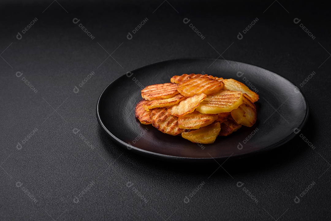 Deliciosas batatas fritas crocantes em fatias em uma placa de cerâmica preta sobre um fundo escuro de concreto