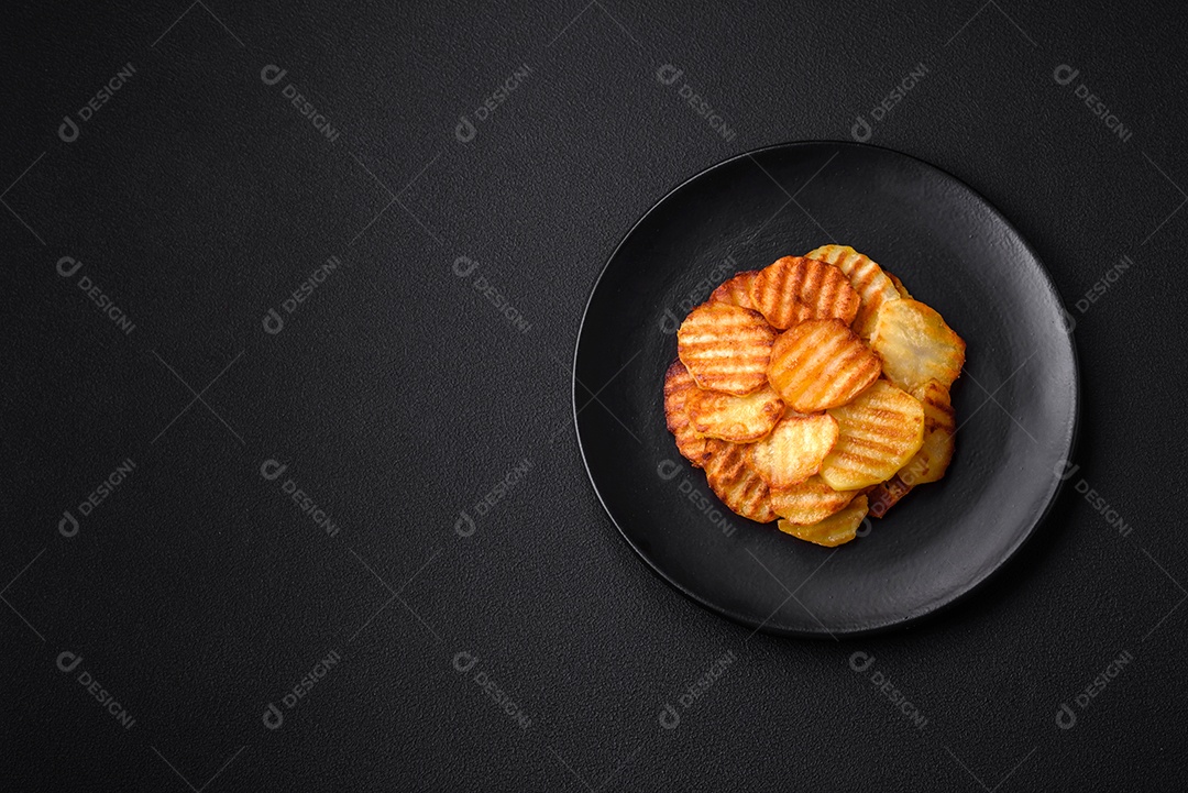 Deliciosas batatas fritas crocantes em fatias em uma placa de cerâmica preta sobre um fundo escuro de concreto